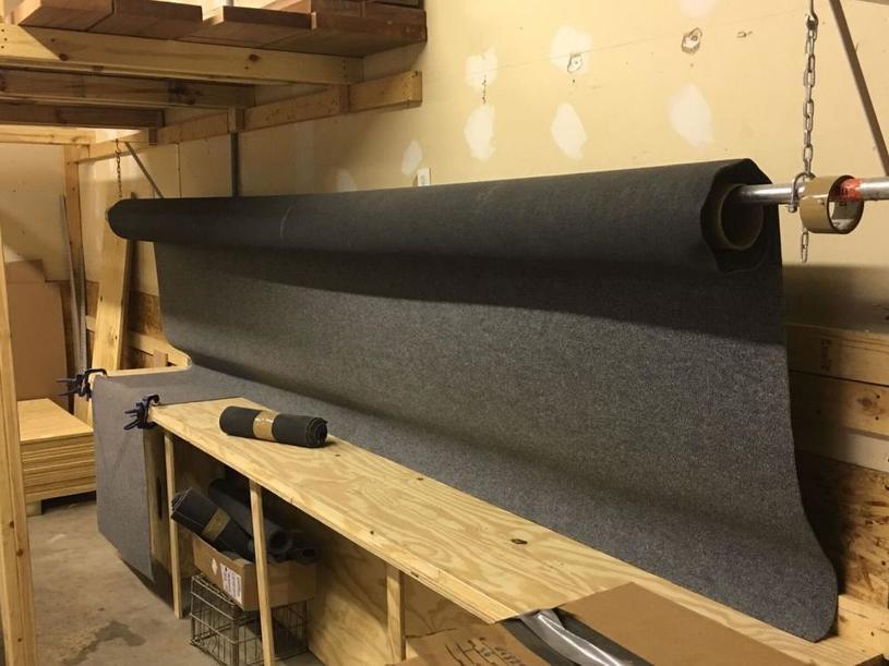 Photo of a large roll of gray fabric on a wooden workbench in a workshop.