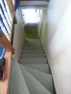 Photo of a narrow, steep staircase with a tight turn at the bottom. The staircase is in a confined indoor space leading to a doorway