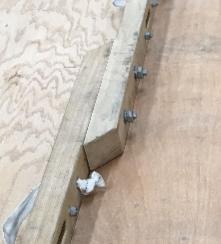 Close-up photo of a wooden piano moving board with metal bolts and handles, placed on a plywood workbench
